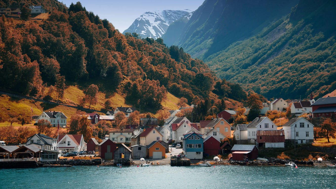 En klynge med hus ved vannet og ved foten av høye, snekledde fjell.