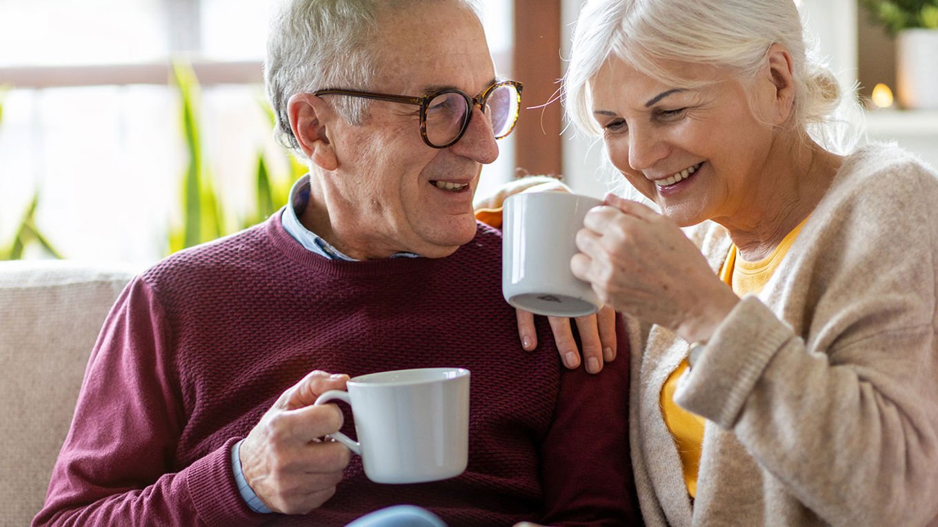 Hvem arver etter deg? Et eldre par i sofaen, med smil og en kaffekopp