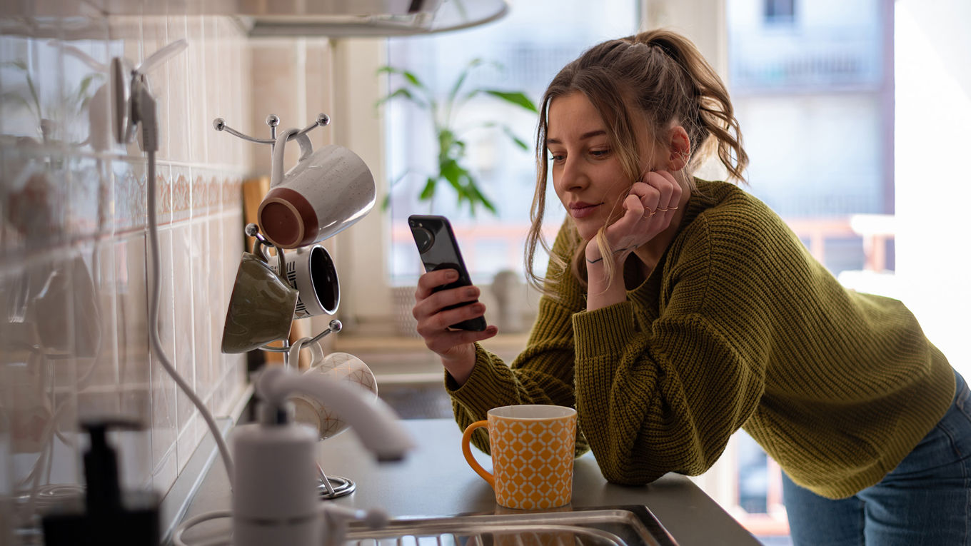 En kvinne i 20-årene står bøyd over kjøkkenbenken og chatter med den juridiske chatboten Lucy.